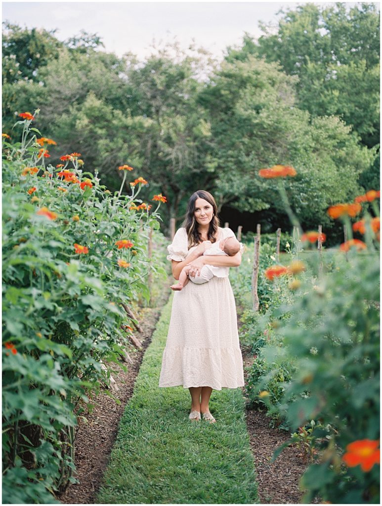 Mother stands in garden holding newborn baby during Richmond family session.