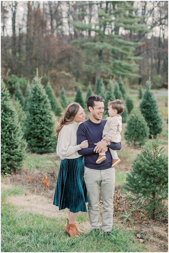 Parents smile and hold their son at Christmas tree farm.