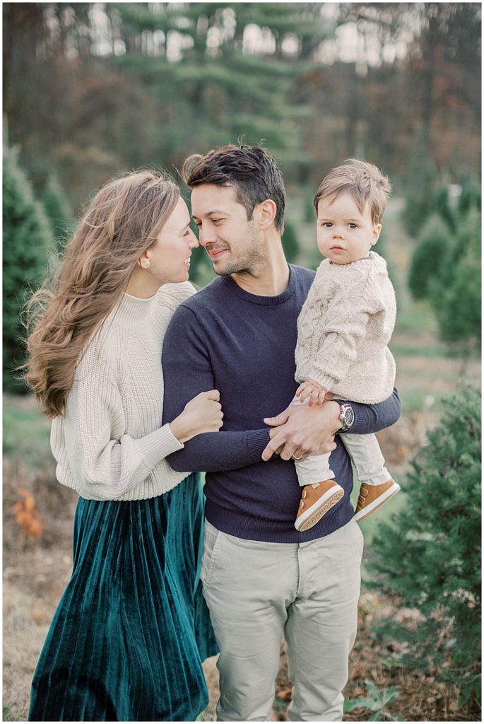 Parents lean in to each other while holding son during Christmas mini sessions at Butler's Orchard.