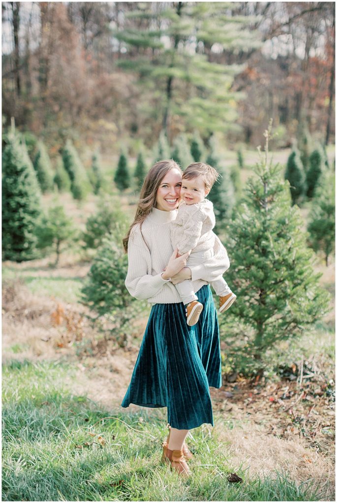 Mother stands with her son at Christmas tree farm.