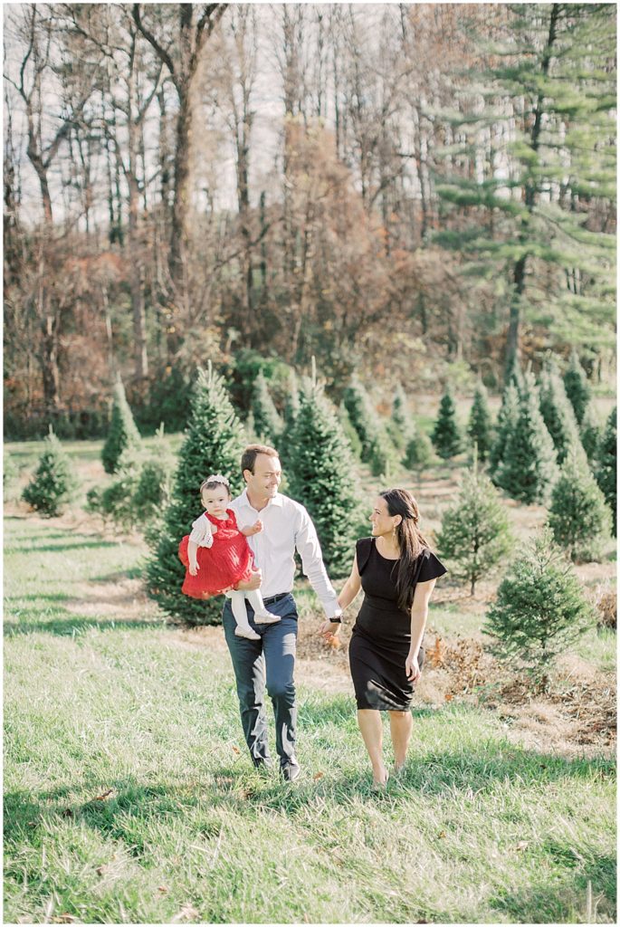 Mother and father walk with their infant daughter at Christmas tree farm.