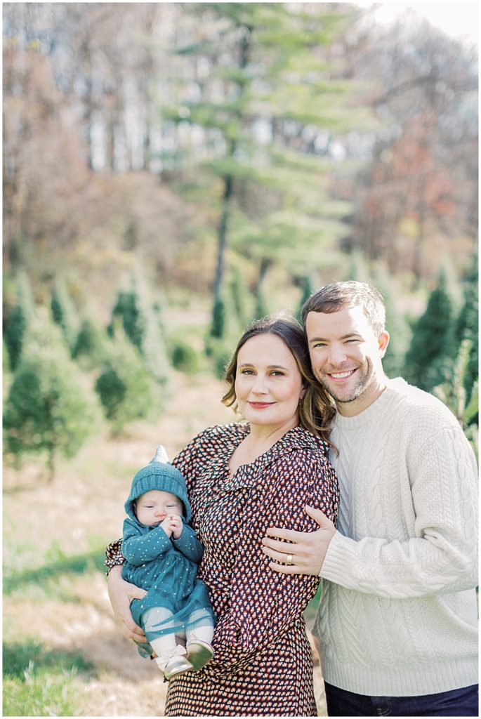 Mother, father, and infant daughter stand together during Christmas mini sessions at Butler's Orchard.
