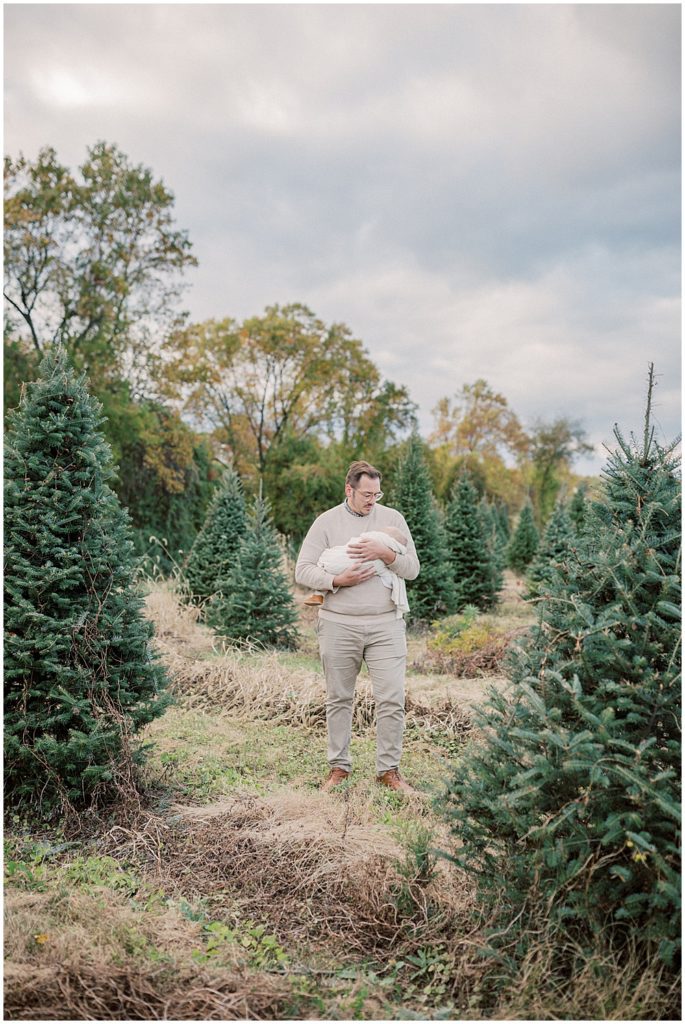 Dad holds newborn baby during Christmas tree farm mini sessions at Butler's Orchard in Maryland.
