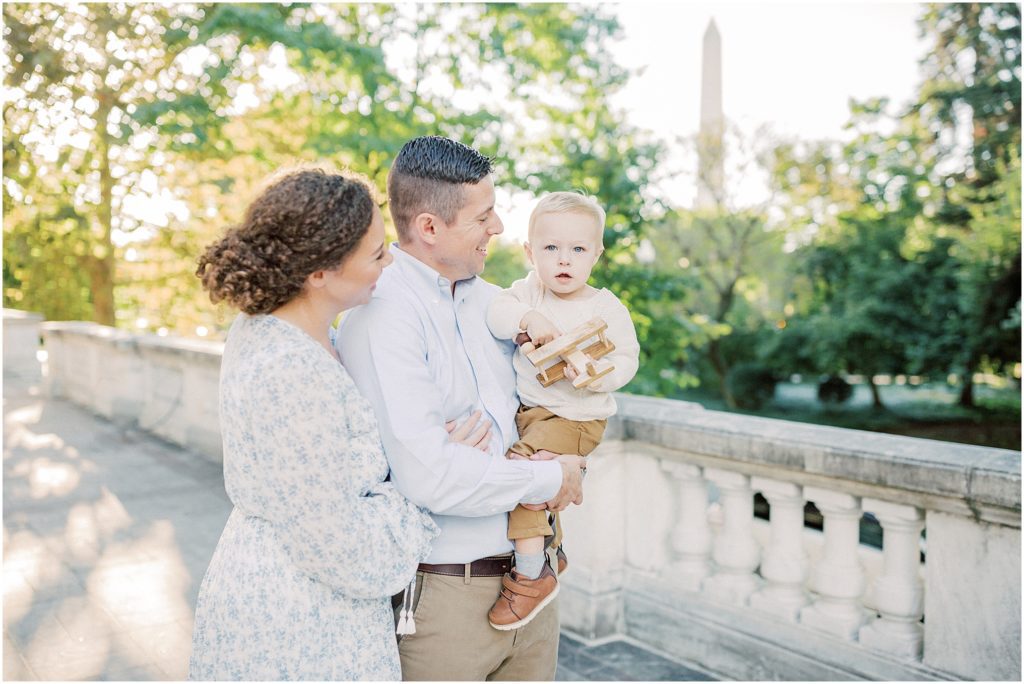 Mother and father hold their toddler son in front of the Washington Monument during DAR Constitution Hall photos for family session.