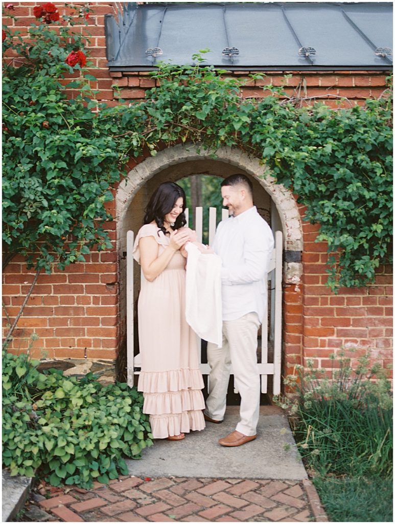 Mother and father smile as they hold their newborn baby under brick archway during newborn session by Loudoun County Newborn Photographer Marie Elizabeth Photography.