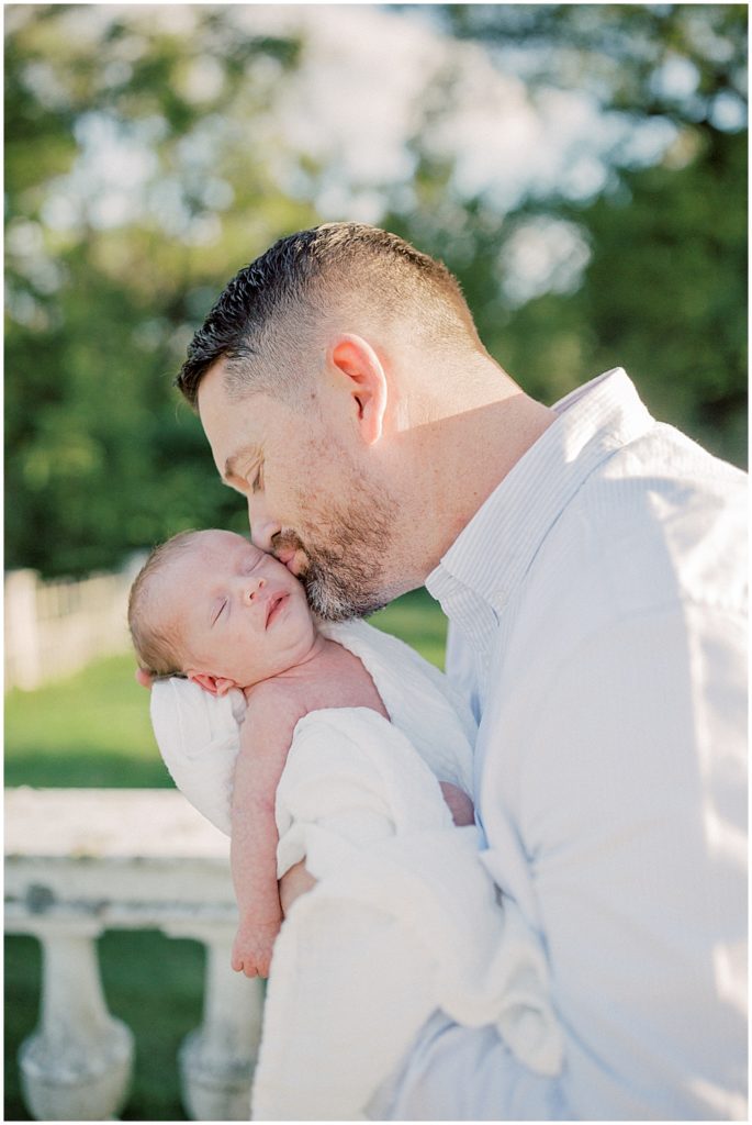 Father leans down and kisses newborn son on the cheek during newborn session by Loudoun County Newborn Photographer Marie Elizabeth Photography.