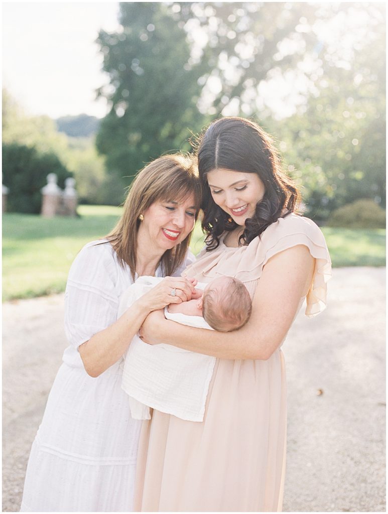 Mother and grandmother hold newborn baby outside at Oatlands Historic Home during newborn session by Loudoun County Newborn Photographer Marie Elizabeth Photography.