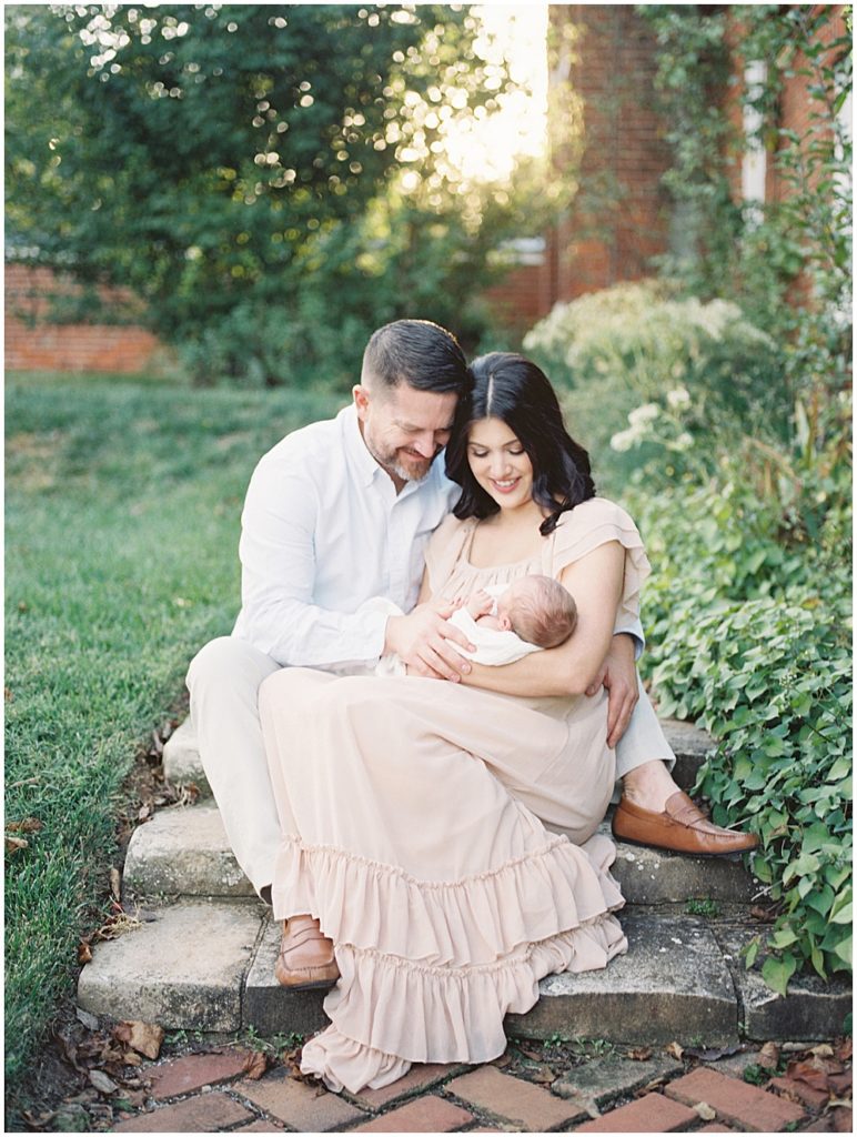 New parents sit on brick steps holding newborn baby at Oatlands Historic Home and Gardens.