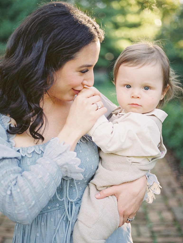 Mother with dark hair kisses her baby's hand, photographed by by Georgetown Family Photographer Marie Elizabeth Photography.