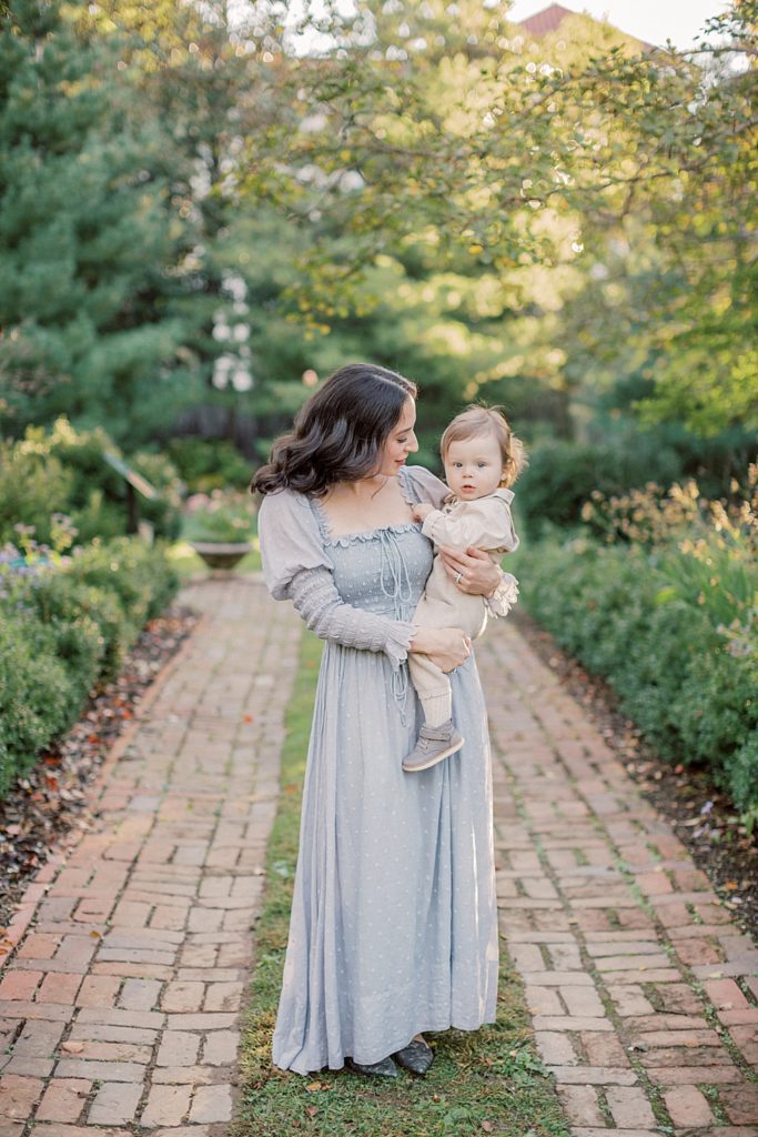 Mother in blue Doen dress holds baby boy down brick lane at Tudor Place DC photographed by Georgetown Family Photographer Marie Elizabeth Photography