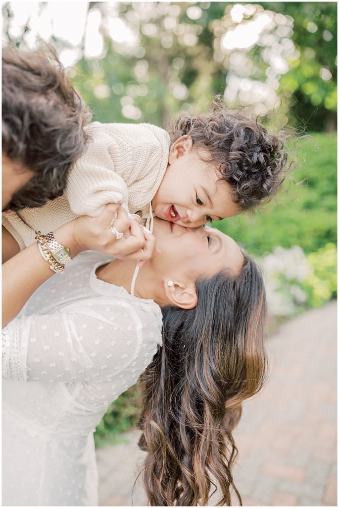 Baby boy is leaned into his mother as he sits on his father's shoulders during extended family session at Green Springs Gardens in Northern Virginia. 