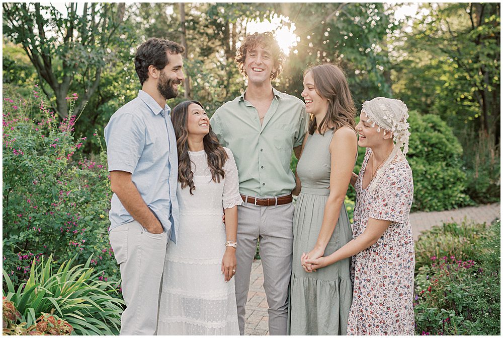 A family of five adults stand, embracing one another, during extended family session at Green Springs Gardens in Northern Virginia. 