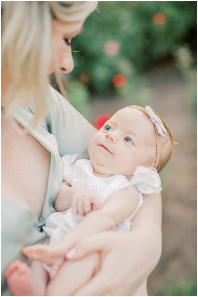 Baby girl looks up at mom with a small smile during outdoor newborn family photos at Bon Air Rose Garden.
