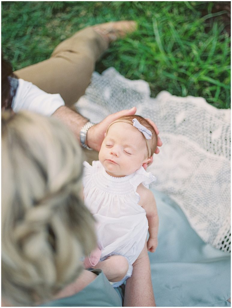 Newborn baby girl sleeps as she is held by her parents during outdoor newborn family photos at Bon Air Rose Garden.