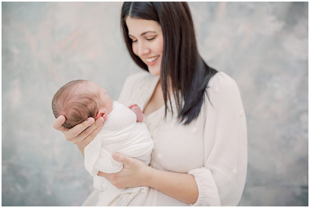 Studio newborn session with brown-haired mother smiling down at her baby.