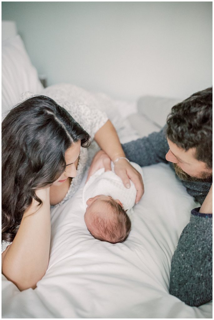 Mother and father lay on bed with baby boy during DC Row House Newborn Session.
