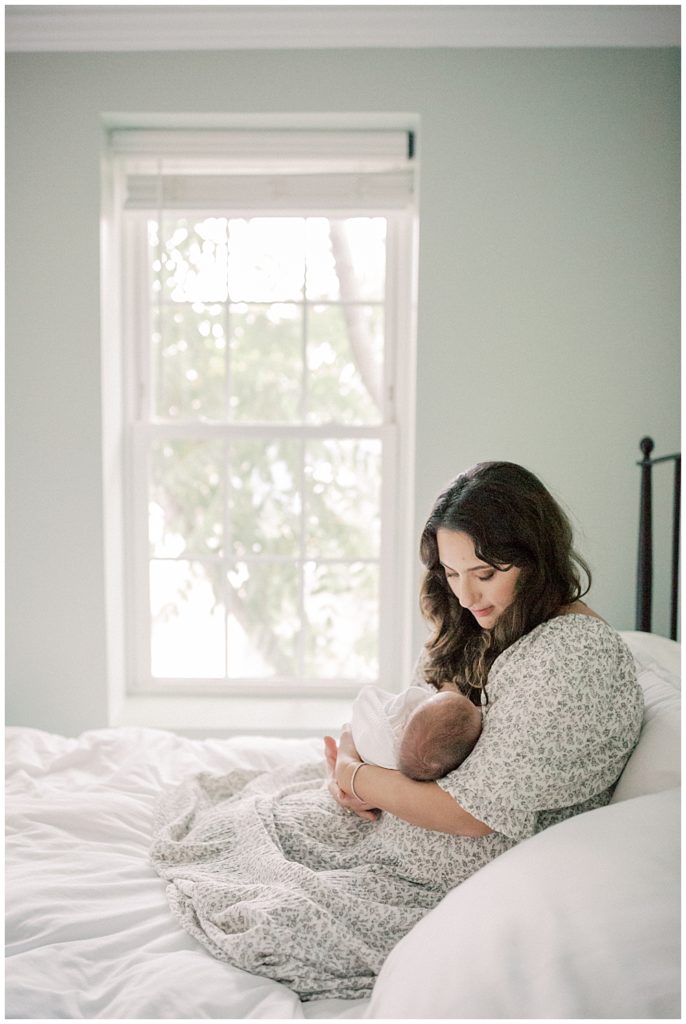 Mother with brown hair sits on bed holding baby boy during DC Row House Newborn Session.