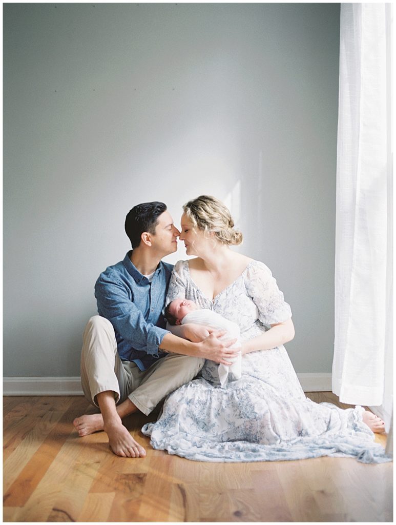 New parents sit on floor, leaning in to one another during Fairfax VA newborn session.