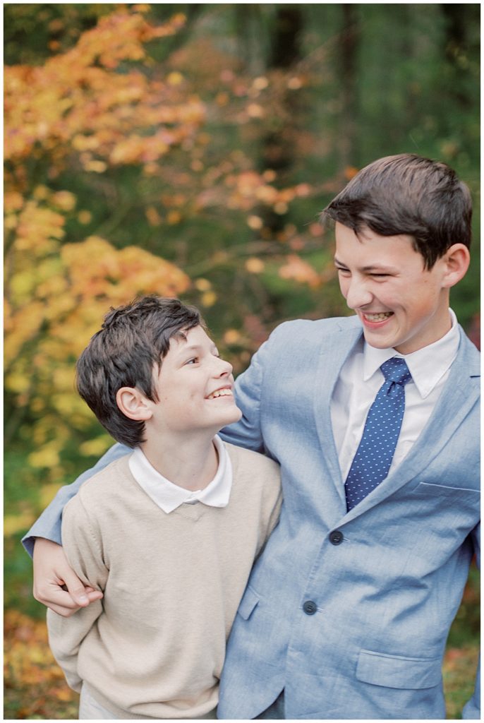 Two middle school boys dressed in a sweater and suit jacket laugh at one another on a fall day.