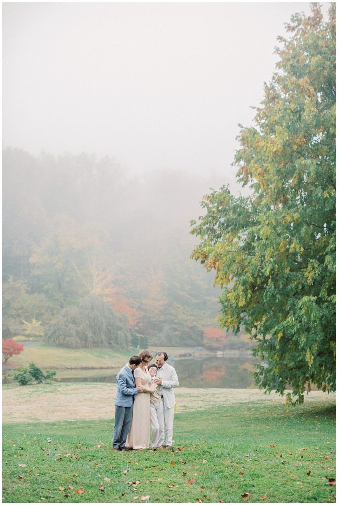 Mother, father, and two young boys stand close together in a foggy field at Brookside Gardens during their family session with older children.