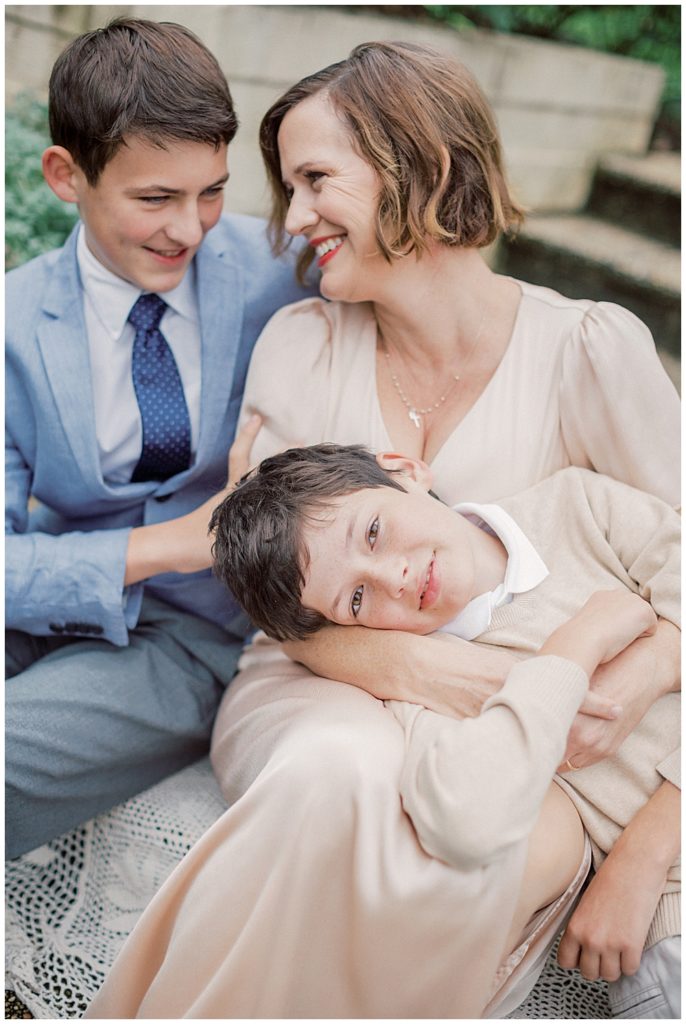 Mother sits with her two sons during their family session with older children, one son sitting next to her in a suit jacket, the other laying on her lap.