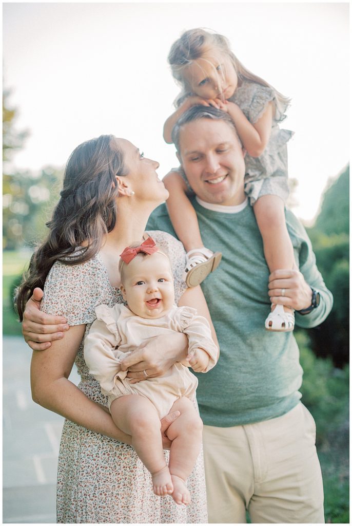 Mother holds baby girl while standing next to husband with toddler girl on his shoulders during Glenview Mansion Photos by Marie Elizabeth Photography