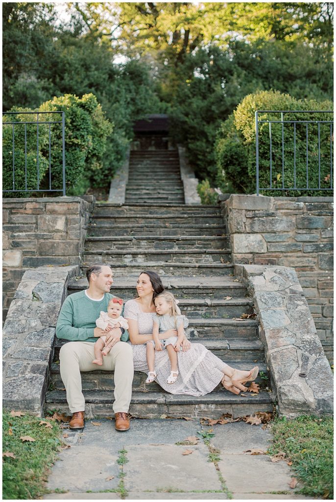 Mother, father, and their two young daughters sit on stone steps during Glenview Mansion Photos by Marie Elizabeth Photography.