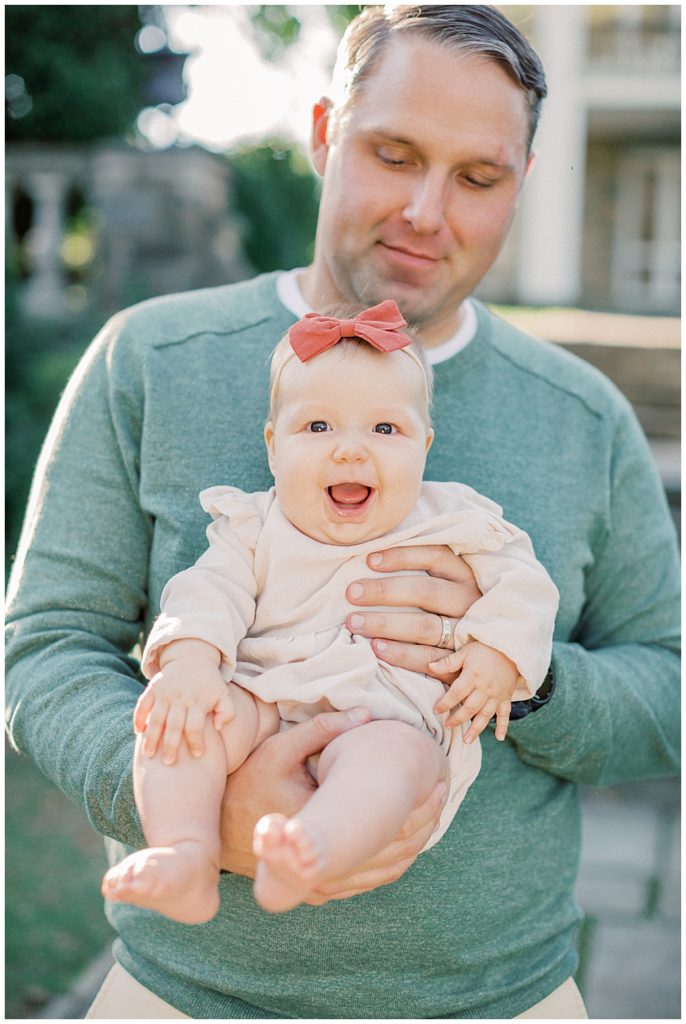 Father holds his baby girl with red bow as she smiles.