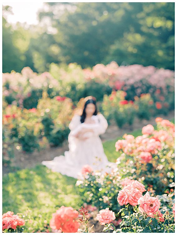 Dark-haired mother sits in the background with roses in the foreground.