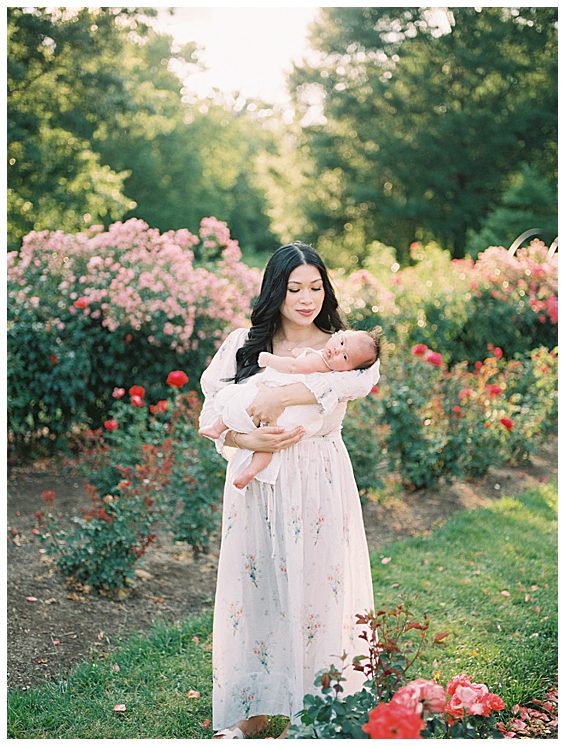 Dark haired mother wearing Doen painted bijou dress holds baby girl in Bon Air Rose Garden photographed by Alexandria Newborn Photographer Marie Elizabeth Photography.