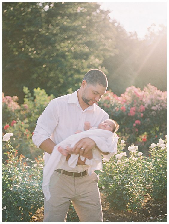 Father holds and rocks his daughter during their outdoor newborn session in Bon Air Rose Garden.
