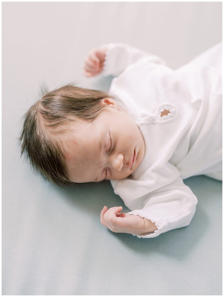 Baby girl in white outfit sleeps on a blue blanket.