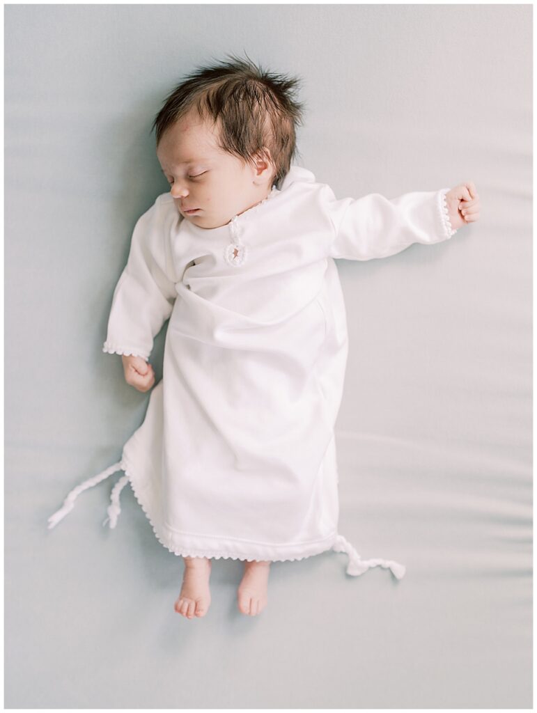 Baby girl in white gown sleeps on blue backdrop.