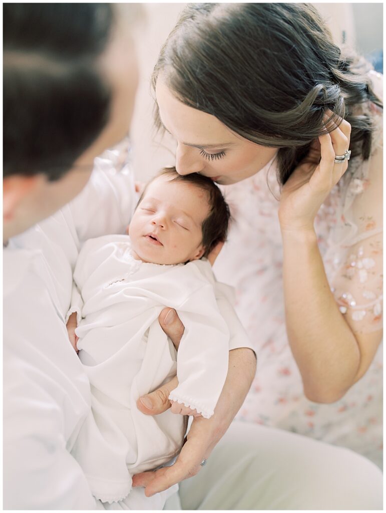 Mother with brown hair leans down and kisses the top of her baby's head while her husband holds baby photographed by Arlington Newborn Photographer Marie Elizabeth Photography.
