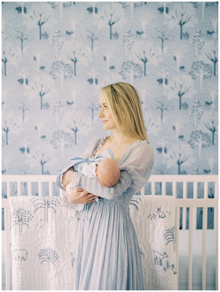 A mother in a blue Doen dress stand holding her baby boy in her Serena & Lily nursery.