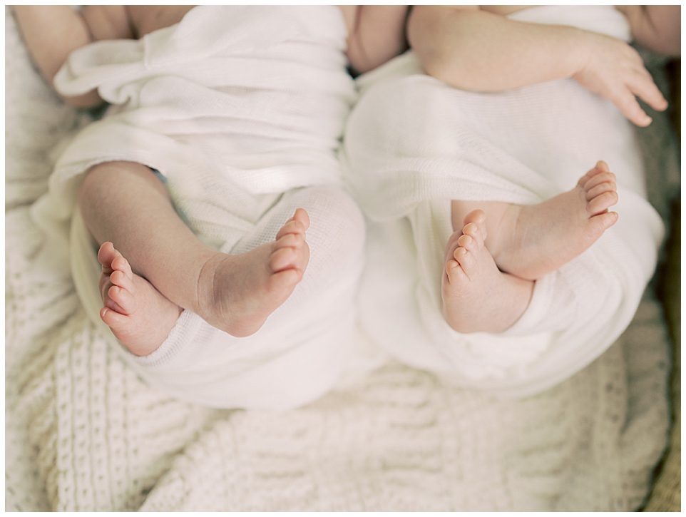 Close-up view of twin baby feet while swaddled in white.
