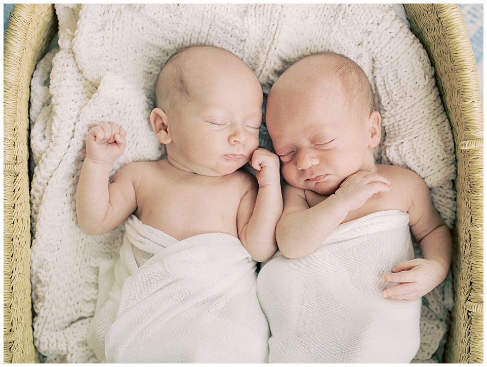 Twin baby boys swaddled in white sleep on a white blanket.