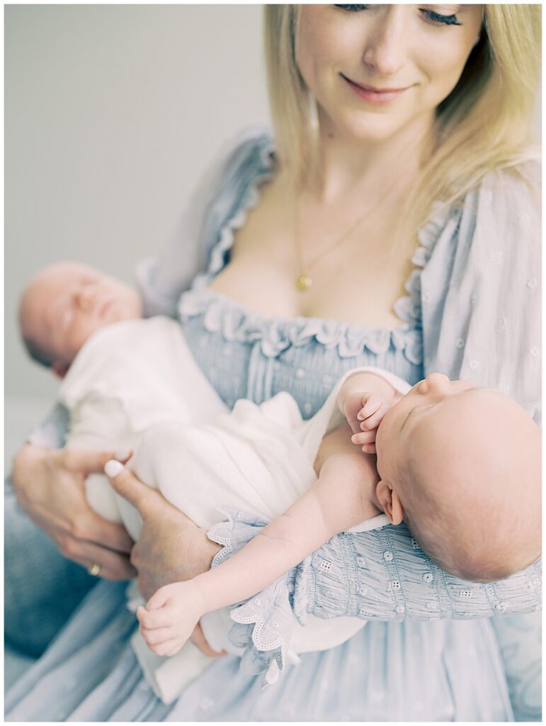 Blonde mother in blue Doen dress holds twin boys and smiles gently down at them during their Chevy Chase newborn session.