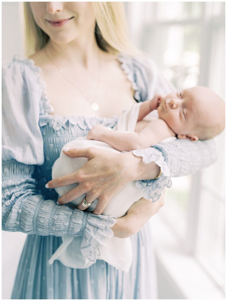 Blonde mother holds her baby boy while wearing a blue Doen dress.