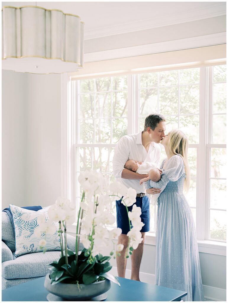 Mother and father lean over to kiss while holding their twin baby boys in their living room during their Chevy Chase newborn session.