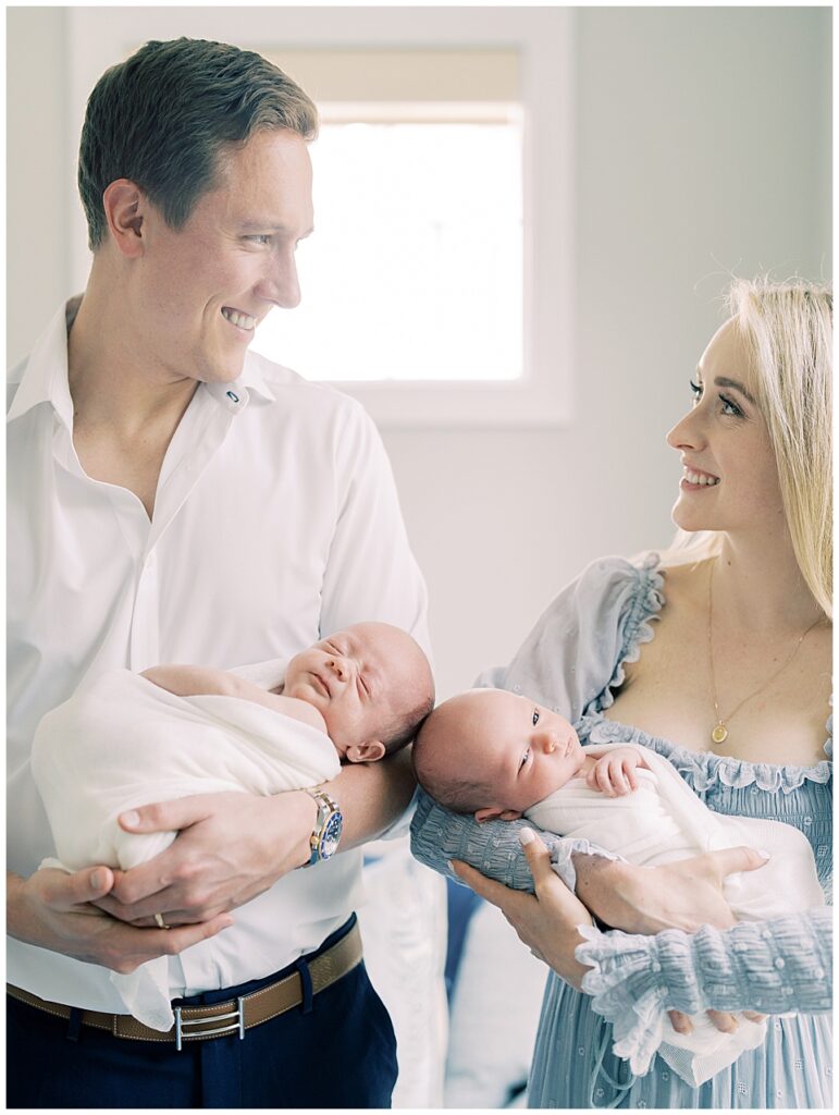 A mother and father hold their twin boys swaddled in white during their Chevy Chase newborn session.