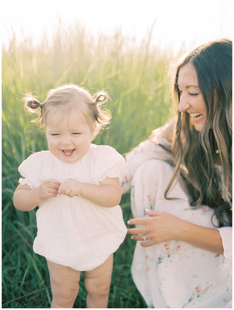 Toddler girl in pigtails laughs as her mother kneels smiling next to her.