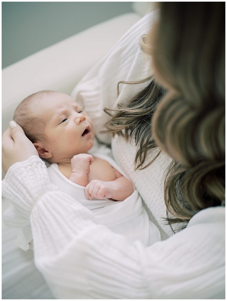 Newborn baby girl looks up at her long brown-haired mother in a white dress.