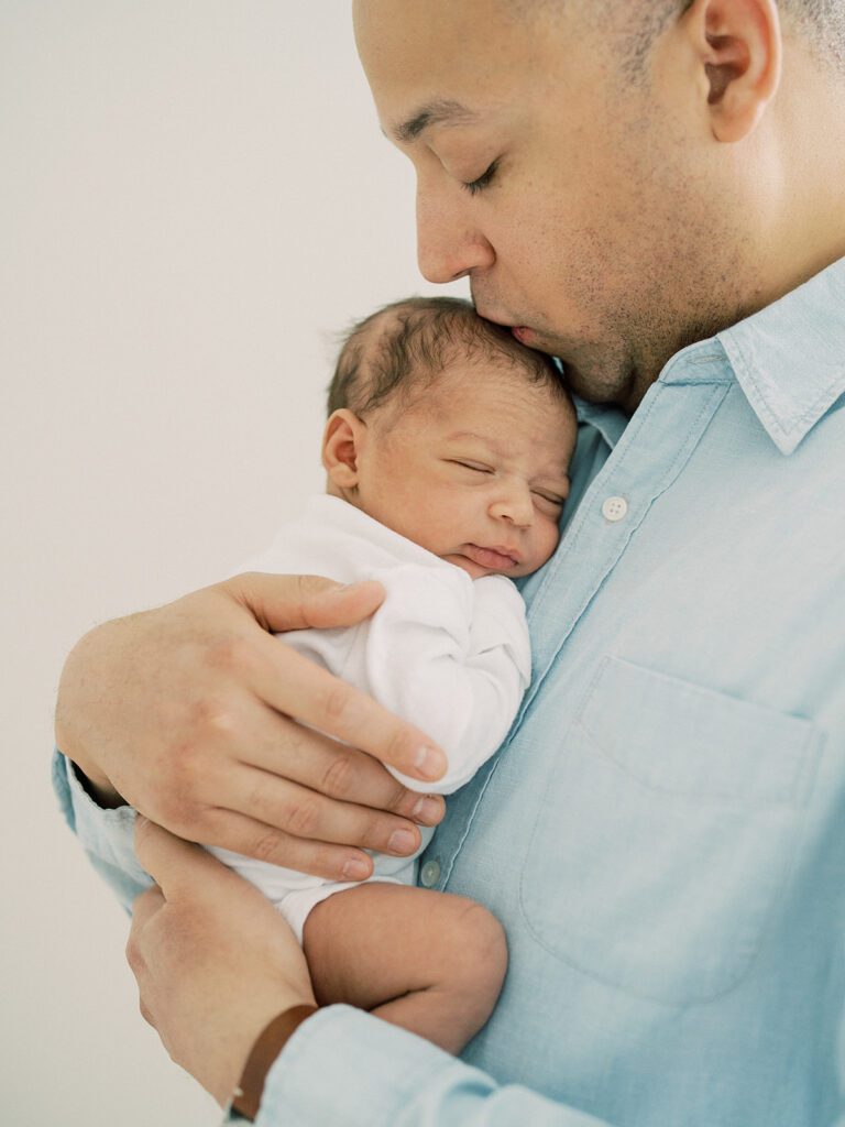 A mixed-race father kisses the top of his newborn son's head.