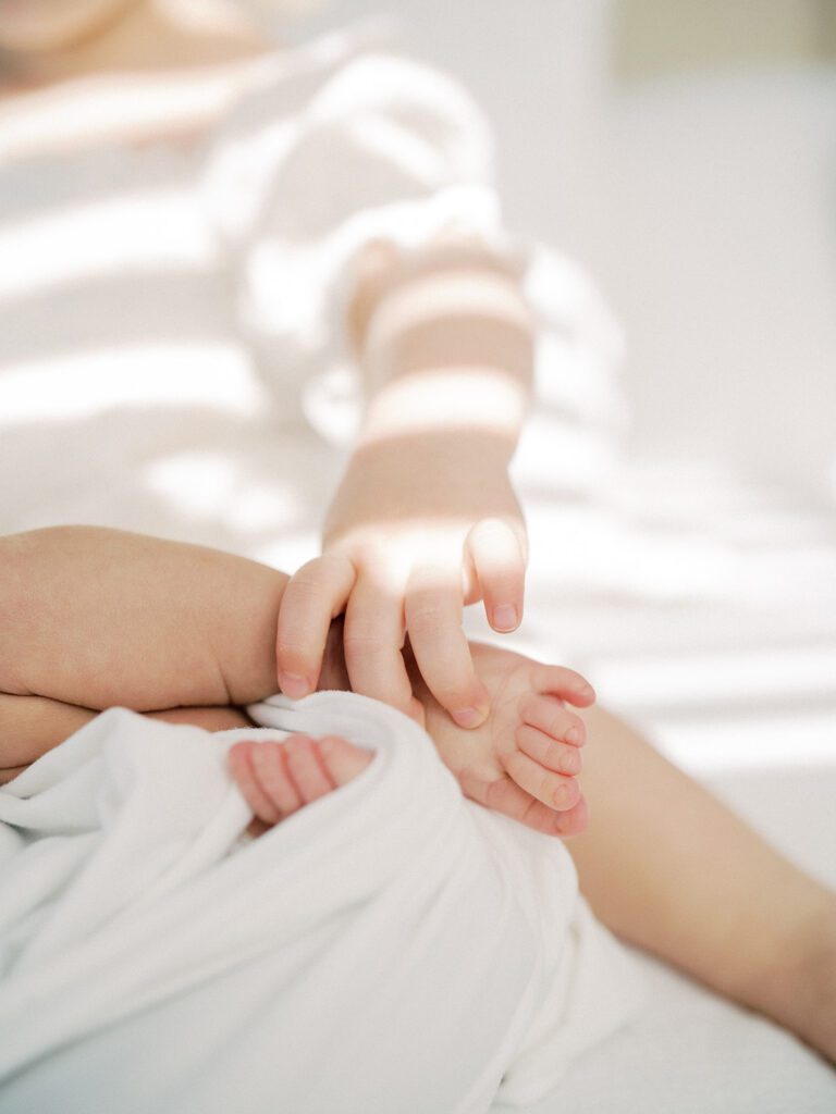 Toddler hand grasps newborn baby foot.