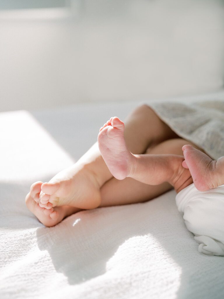 Newborn and toddler feet dangling from a bed.