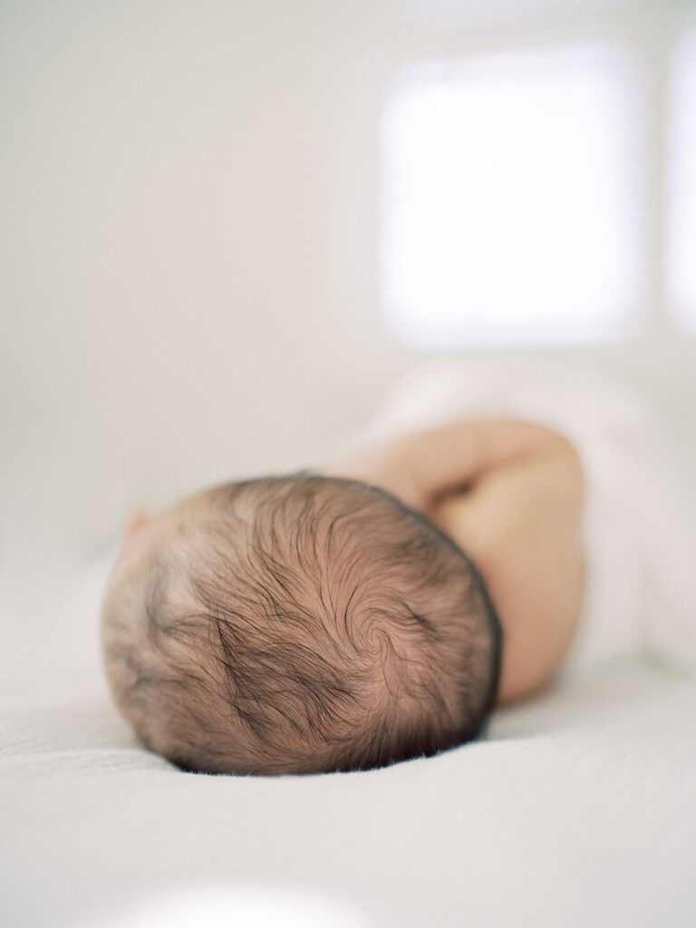 Close-up view of baby's hair as newborn baby lays on white bed.