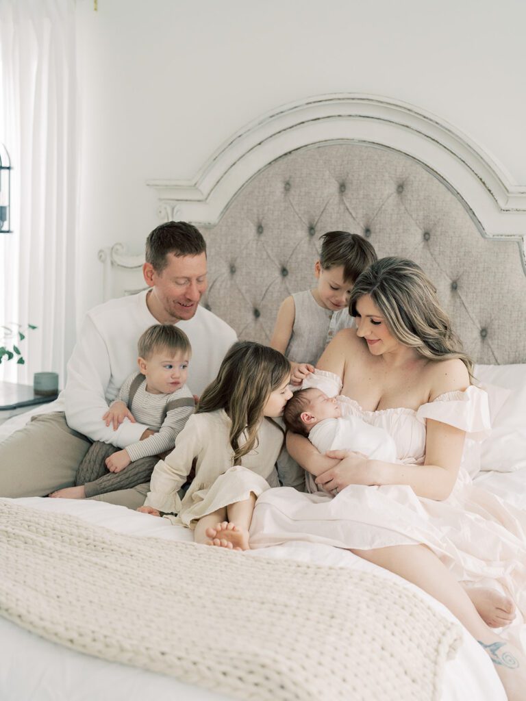 Mother and father sit on bed with three young children and their newborn baby during their newborn photos in Annapolis.