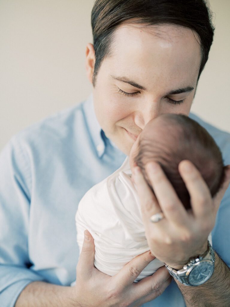 Father with brown hair leans down to nuzzle his newborn son.