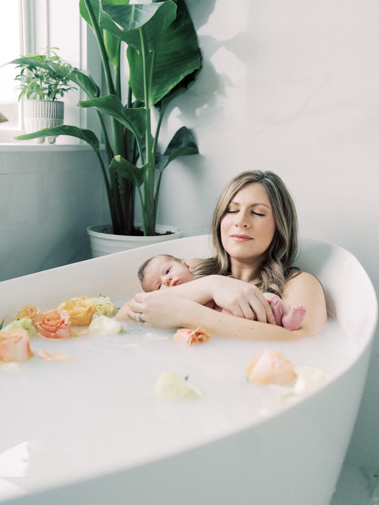 A milk bath photoshoot with a mother and baby in a tub full of flowers.